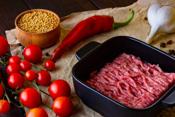 Minced meat on craft paper which lies on a wooden light table. Red hot chili peppers together with peppercorns