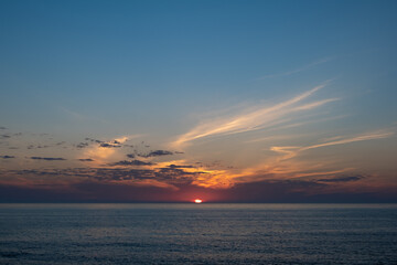 Wide view over ocean at sunset with vivid colorful sky and dramatic clouds on horizon