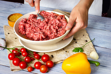The process of cooking cutlets on a light wooden table from minced pork. Female hands sprinkle seasoning and pour olive oil over minced meat. Make cutlets
