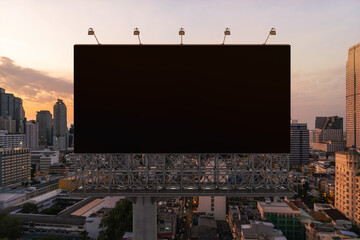 Blank black road billboard with Bangkok cityscape background at sunset. Street advertising poster, mock up, 3D rendering. Front view. The concept of marketing communication to promote or sell idea.