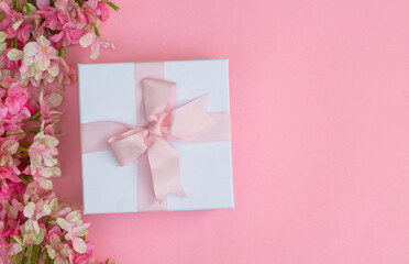 Pink flowers and a gift box on pink background. Space for text