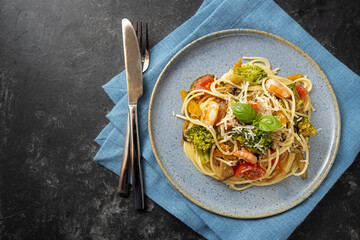Spaghetti pasta with vegetables and shrimps, Mediterranean meal on a blue plate and a dark rustic background, copy space, high angle view from above