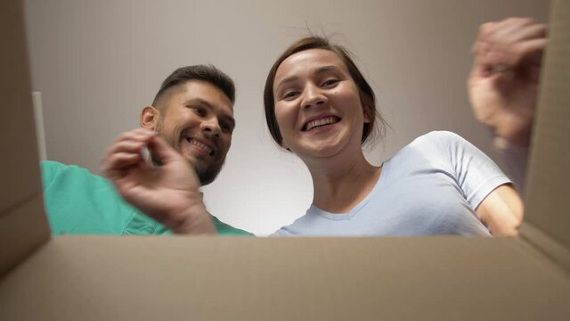 Happy woman and man couple open delivery internet shopping box, smiling woman looking inside e-commerce clothes delivery, wow effect
