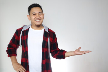Young Asian man smiling, showing and pointing something on his side, against white wall with copy space