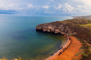 Obraz premium Landscape of the morning sea coast. The turquoise surface of the calm sea. Picturesque dark clouds in the blue sky. Picturesque coastal cliffs. Tourism and travel.
