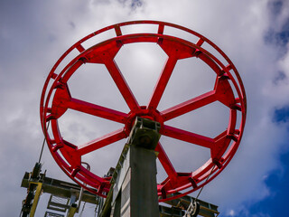 Huge red circle shape ski lift gear against cloudy blue sky.