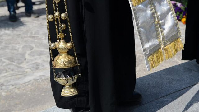 A priest swings a thurible on missal. Orthodox priest with hand censer during worship service. Censer used during liturgy. Man swinging chain censer. 