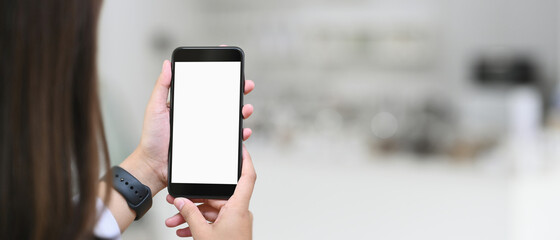 Cropped shot woman holding mockup smartphone in blurred cafe.