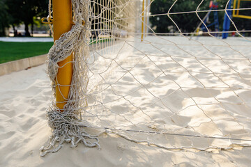 Net fence around the beach volleyball court, iron post for attaching the mesh, white fine sand, sunlight, background.