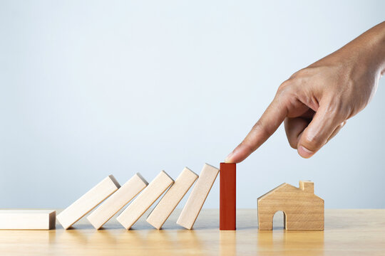 Finger stopping the domino falling over the house. Real estate investment concept. Business strategy