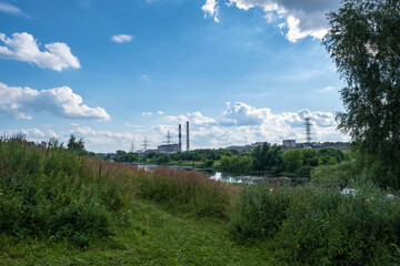Obraz premium City landscape with the Uvod river with a power line and high pipes on a sunny summer day.