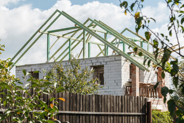 The process of building a house behind a wooden fence. Structure of brick and aerated concrete. Wooden rafters on the house