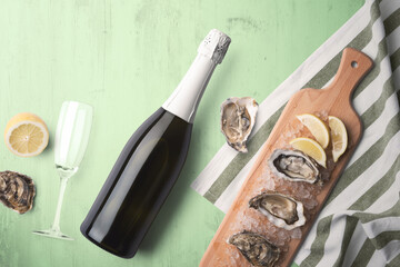 An unopened champagne bottle with a single glass on a green tinted wooden background with fresh oysters and lemon on a wooden cutting board