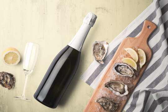 An unopened champagne bottle with a single glass on a yellow tinted wooden background with fresh oysters and lemon on a wooden cutting board