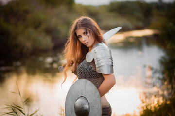 Portrait of a medieval woman warrior in chain mail with a sword and shield in her hands against the...