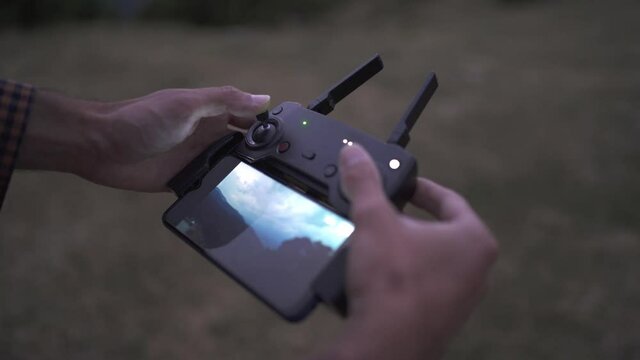 Drone Remote Controler used with a mobile phone. Drone pilot hands controlling a drone while flying it in a valley