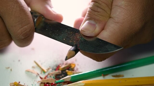 Footage of hands slowly sharpening a pencil and some coloured pencils with a sharp knife.