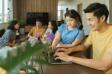 Young Asian father use laptop work at home with big family mom ,daughter ,grandfather grandmother...