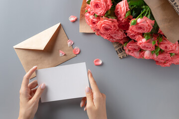 woman's hands holding a blank white card on the background of a bouquet of pink roses. Holiday...