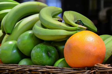 Close-up of fruits in a smoothie basket at a food market: green bananas, apples, ripe grapefruit. Fresh organic fruits on the market.