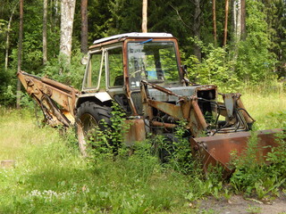 Fototapeta na wymiar Rusty abandoned tractor in the grass at the edge of the forest