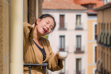 young happy and beautiful Asian Korean woman enjoying city view from hotel room balcony in Spain during holidays trip in Europe drinking coffee smiling cheerful i