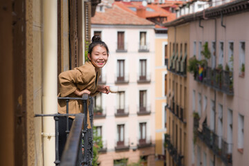 Obraz na płótnie Canvas young happy and beautiful Asian Chinese woman enjoying city view from hotel room balcony in Spain during holidays trip in Europe drinking coffee smiling cheerful