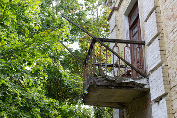 Old rusty balcony on brick building wall  among green foliage in sunny day