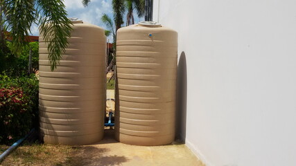 Outdoor cream colored plastic water bucket. Two water buckets are mounted on a concrete base beside the house wall to reserve water for use and copy space. Selective focus
