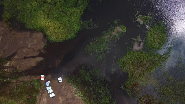 Lago grande con lanchas en medio de un bosque rodeado de arboles verdes con una carretera a un costado donde pasan carros
