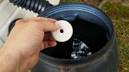 hand holding mosquito tablet insecticide over rain barrel