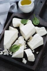 Black wooden serving tray with chunks of feta cheese, close-up, vertical shot, selective focus