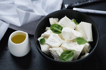 Black bowl with chunks of feta cheese, fresh spinach leaves and olive oil, horizontal shot on a black stone surface
