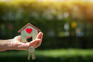 Investor hand holding the home with red heart and house key in the public park, Saving for buy real estate for business investment concept.