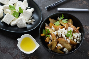 Greek style baked potato wedges served with feta cheese and olive oil, studio shot over brown stone background