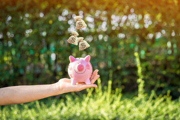 Women hands hold a piggy bank and money bag dropping on the top in the public park for loans to planned investment in the future concept.