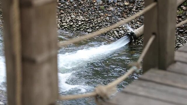 Water is poured out with a strong pressure from a rubber pipe. View over a wooden bridge