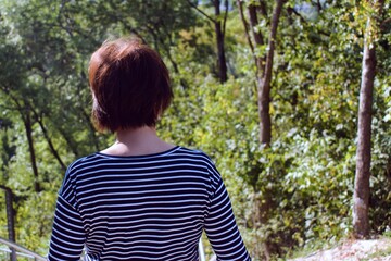 Fototapeta premium girl in striped T-shirt on blurred background of green forest. view from the back