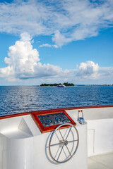 The deck of the ship with the steering wheel on the background of an uninhabited tropical island in...