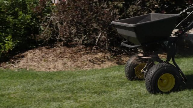 Lawn technician using a push spreader. Using manual push spreader at the lawn.