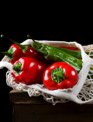 Peppers of different sorts in the mesh bag against the black background