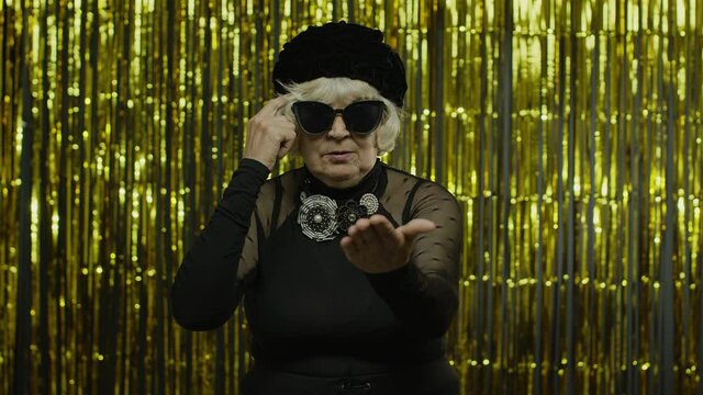 Displeased annoyed senior old woman showing stupid gesture. Elderly grandma on yellow background
