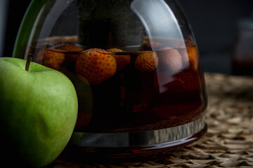 Turquoise mug with tea. Glass teapot with berry tea. Green apple. Still life on a dark table.