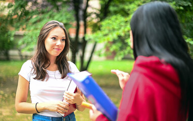 Two female schoolmates talking in a college courtyard