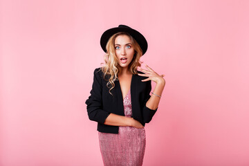  Girl with surprise face standing over pink background . Wearing elegant dress with sequins . Amazed emotions.Wearing trendy dress with sequence , black jacket and hat.