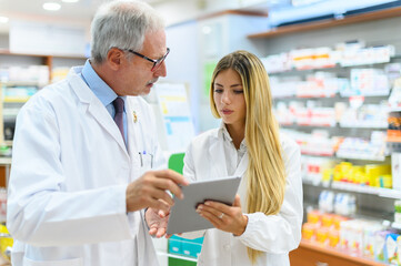 Two pharmacists talking while working on tablet in their store