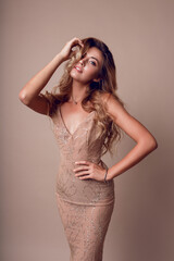 Happy graceful woman with blonde wavy hairs posing in studio. wearing elegant beige sequins  dress.