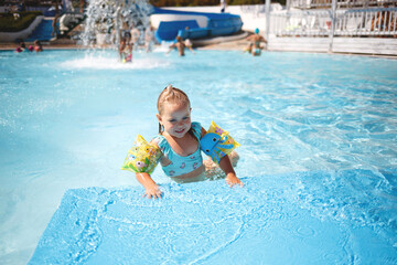 little girl swims in the pool in the outdoor water park