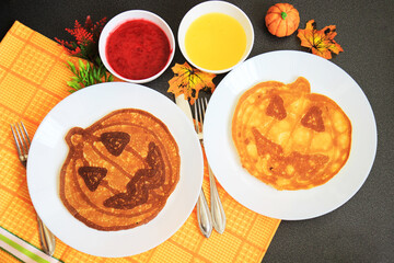 Halloween breakfast. pancakes in the form of a pumpkin-lantern on white plates, served with honey and cranberry jam