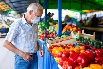 retired european man wearing medical mask protecting against virus buying tomatoes in market